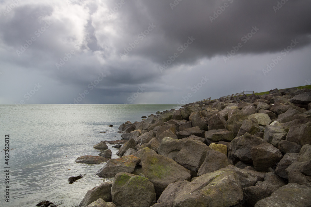 Toe protection of a solid sea dike, made of heavy boulders, under dark, threatening sky