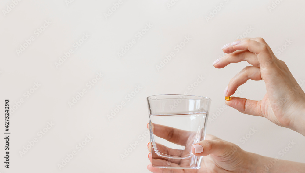 Feminine hands holding glass of water and yellow capsule of vitamin d3 or fish oil omega Feminine hands holding glass of water and yellow capsule of vitamin d3 or fish oil omega