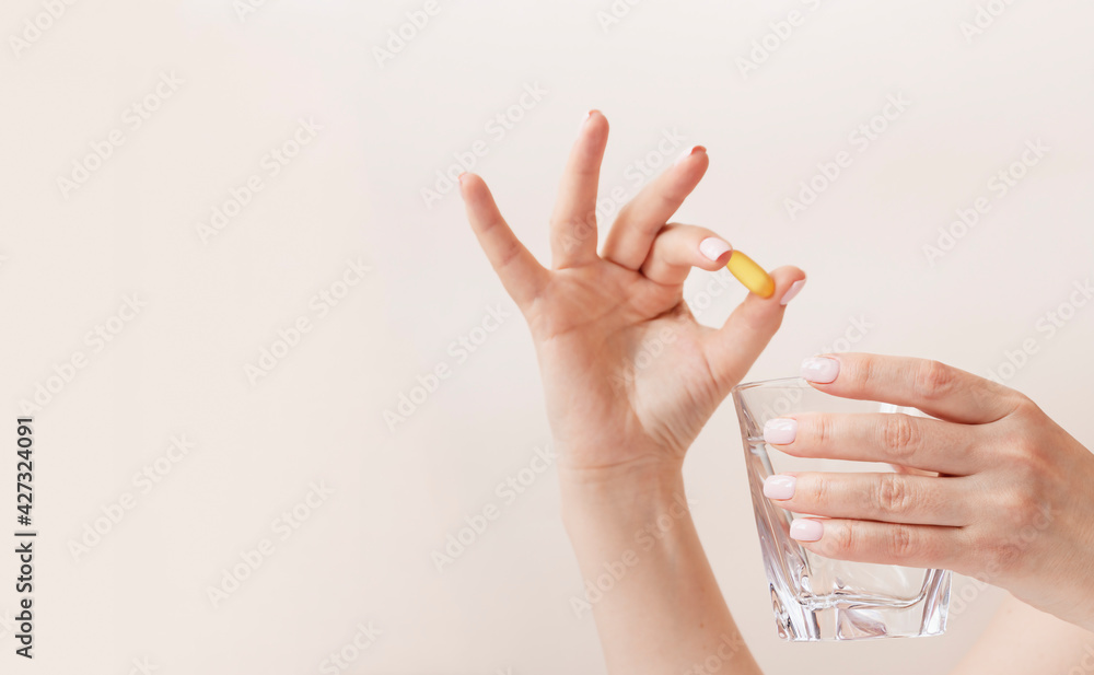 Feminine hands with trendy manicure holding glass of water and yellow capsule of vitamin d3 or fish oil omega Feminine hands with trendy manicure holding glass of water and yellow capsule of vitamin d3 or fish oil omega
