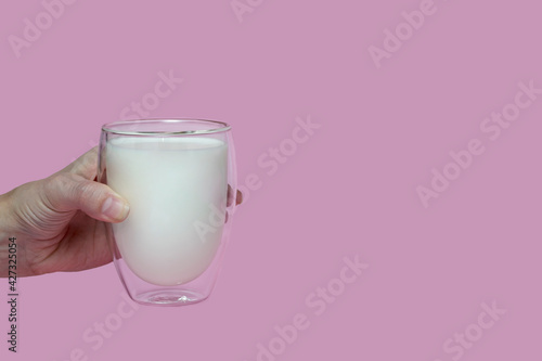 female hand holding a glass with fresh milk, on a pink background,fortified drink, calcium © Tasha