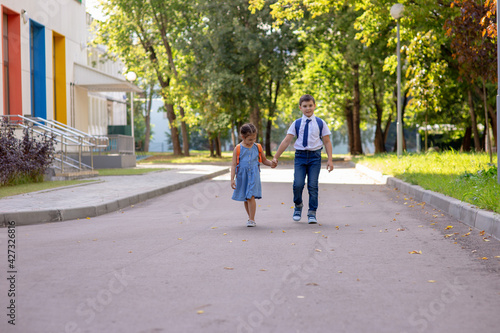 Cheerful schoolchildren, a little girl and a boy in a white shirt with backpacks, go from school.