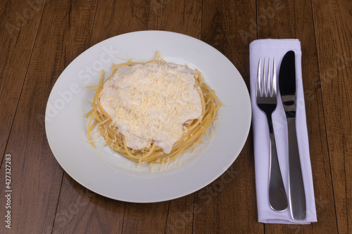Pasta with bechamel sauce with grated cheese on top. Spaghetti with white sauce served on the white plate. Photograph of typical Italian and French food with centralized elements.