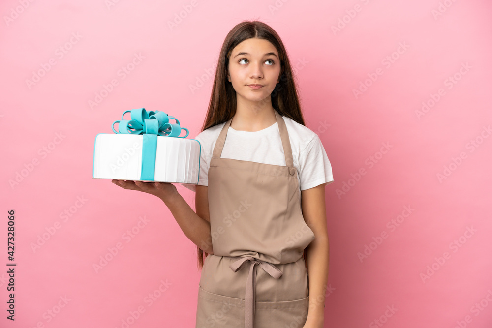 Little girl with a big cake over isolated pink background and looking up Little girl with a big cake over isolated pink background and looking up