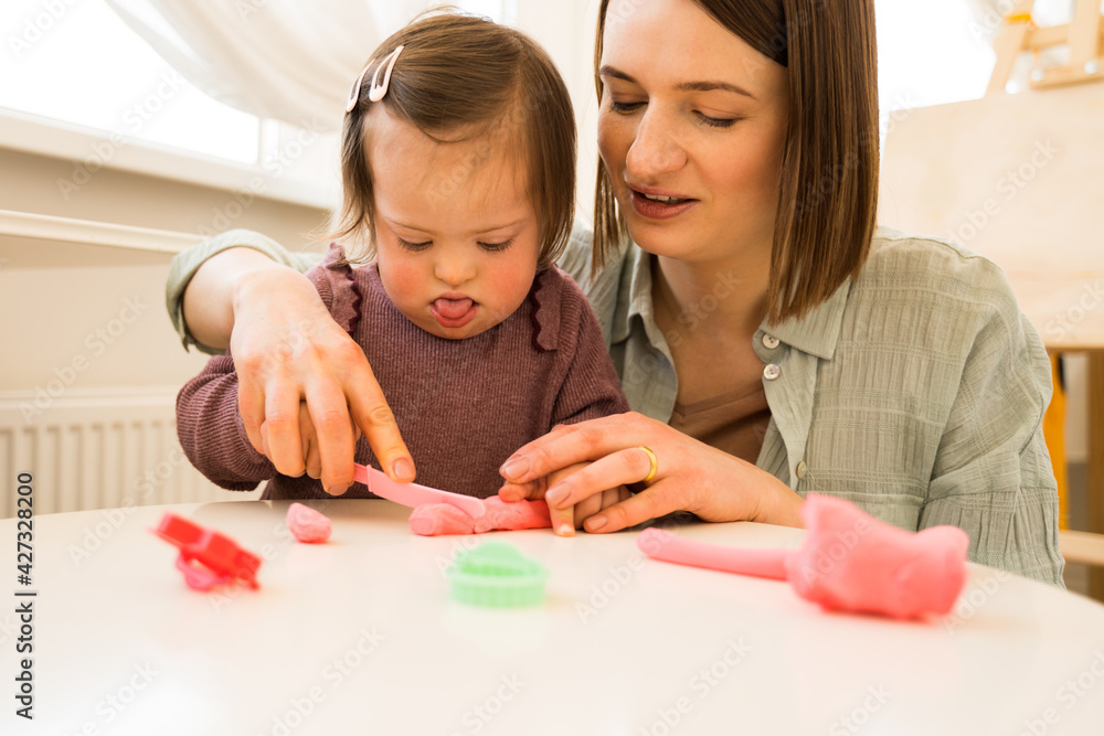 Fototapeta premium Girl with down syndrome sculpturing from the plasticine at the table