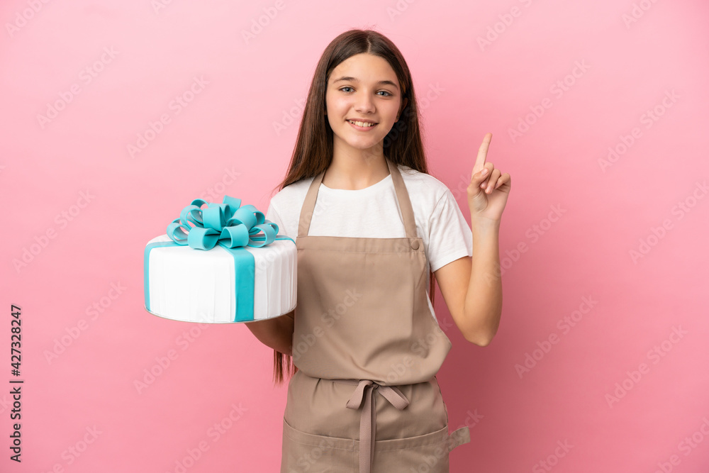 Little girl with a big cake over isolated pink background showing and lifting a finger in sign of the best Little girl with a big cake over isolated pink background showing and lifting a finger in sign of the best