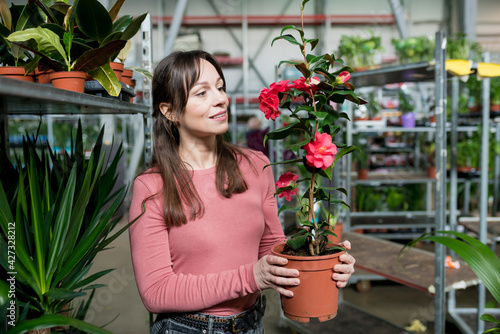 Young smiling woman choosing houseplants in garden centre. Female person shooping flowers for home in plant nursery
