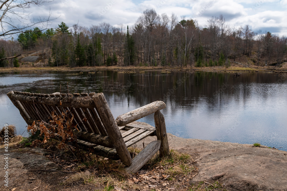 A lone bench sits idle overlooking a lake on Cooper's Falls Trail in the Muskoka region of Ontario on an early-spring day before the leaves return to the trees.