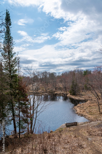 A lone bench sits idle at the bottom of a hill overlooking a lake on the Cooper's Falls Trail in Muskoka, Ontario on a partially cloudy day.