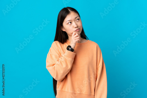 Young Chinese girl over isolated blue background and looking up