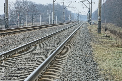 Railway track with rails and sleepers, covered with gray stones and brown grass