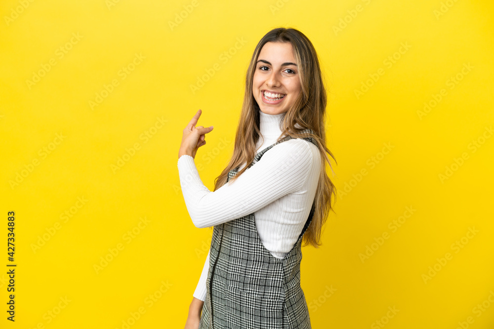 Young caucasian woman isolated on yellow background pointing back Young caucasian woman isolated on yellow background pointing back
