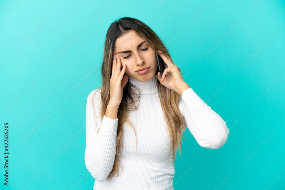 Young caucasian woman using mobile phone isolated on blue background with headache Young caucasian woman using mobile phone isolated on blue background with headache