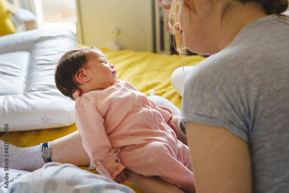 Unknown caucasian woman holding her newborn baby two weeks old at home - infant girl in arms of her mother feeling safe sleeping or taking a nap - childhood growing up and parenthood concept