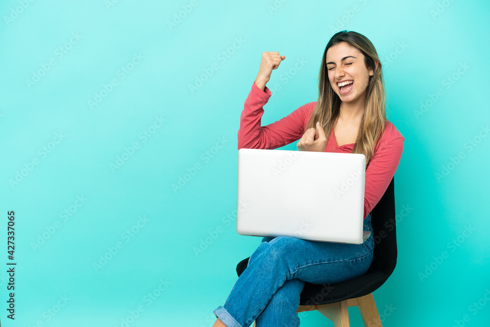 Young caucasian woman sitting on a chair with her pc isolated on blue background celebrating a victory Young caucasian woman sitting on a chair with her pc isolated on blue background celebrating a victory