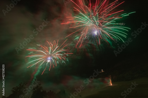 Awesome fireworks with italian flag colors lighting sky over trees silhouette and over an illuminated church, Vittorio Veneto, Italy