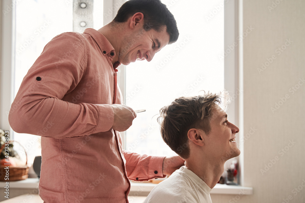 Homosexual couple cutting their own hair at home with a comb and scissors Homosexual couple cutting their own hair at home with a comb and scissors