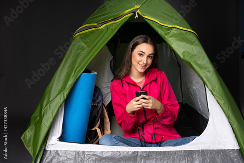Young caucasian woman inside a camping green tent sending a message with the mobile