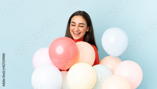 Young woman catching many balloons isolated on blue background
