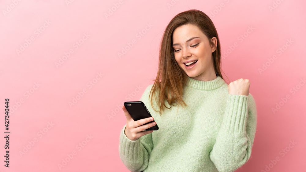 Teenager girl over isolated pink background with phone in victory position Teenager girl over isolated pink background with phone in victory position