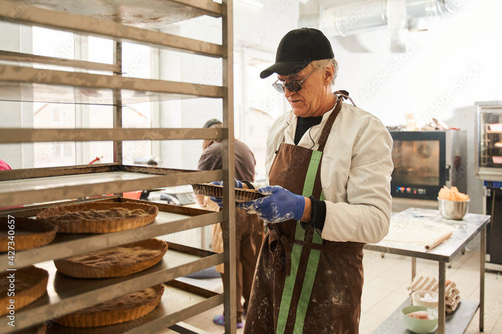 Male worker putting pies on tray on a bakery trolley Male worker putting pies on tray on a bakery trolley