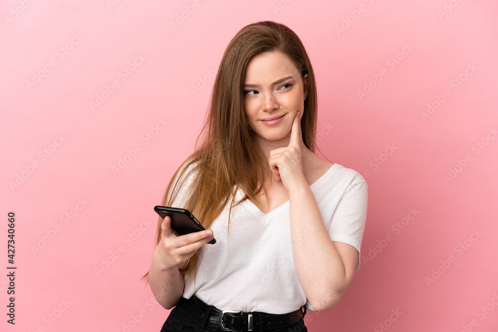 Teenager girl over isolated pink background using mobile phone and thinking Teenager girl over isolated pink background using mobile phone and thinking