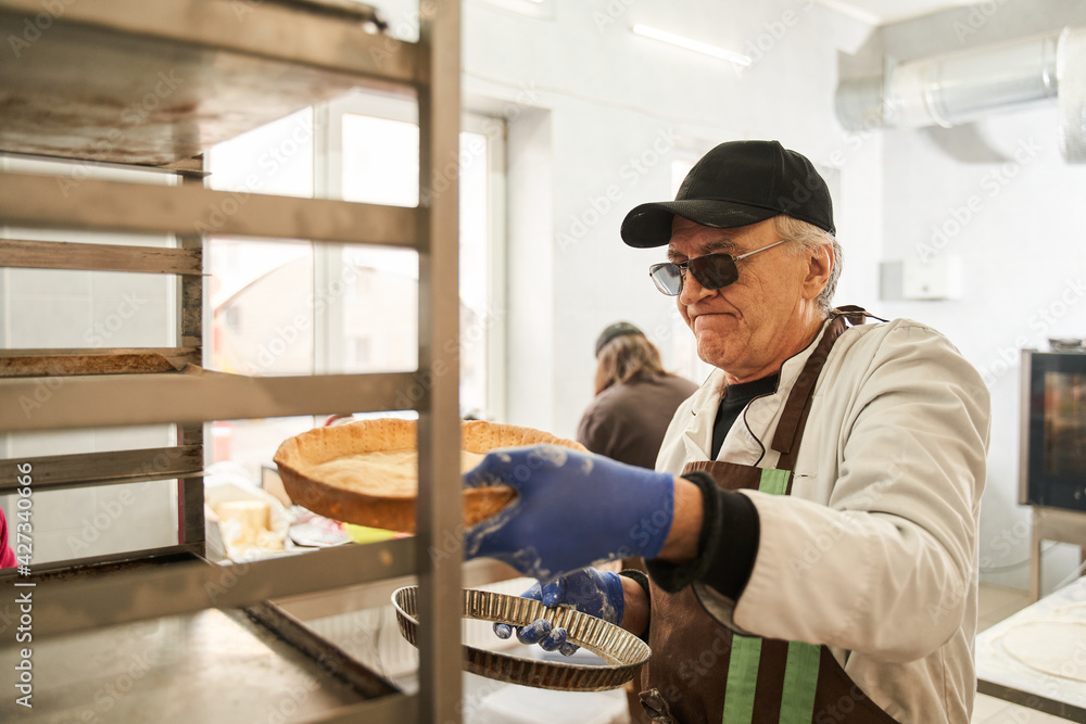 Male worker putting pies on tray on a bakery trolley Male worker putting pies on tray on a bakery trolley