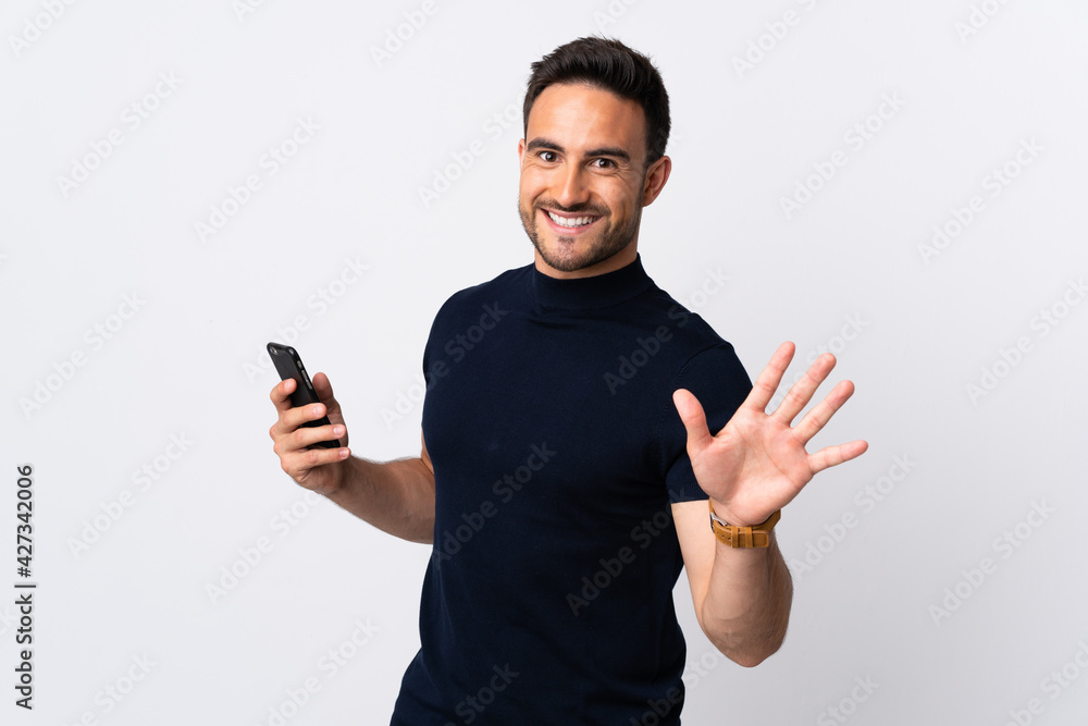 Young caucasian man using mobile phone isolated on white background saluting with hand with happy expression Young caucasian man using mobile phone isolated on white background saluting with hand with happy expression