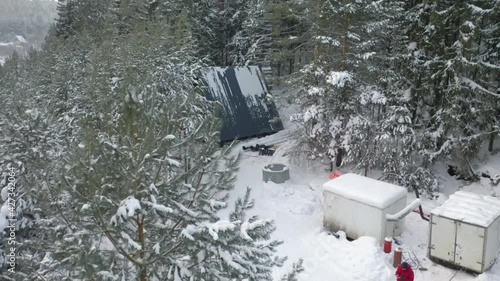 Aerial view of a winter camp located deep in winter forest and a male hiker in warm clothes. Clip. Small house built among snow covered spruce trees. photo