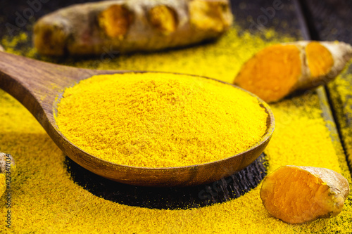 spoonful of turmeric powder, turmeric roots in a wooden bowl