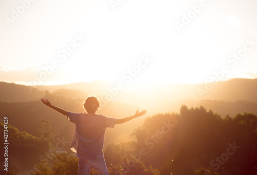 Man with arms raised on top of a mountain with the sunset in the background. Concept of happiness, mental well-being and success.