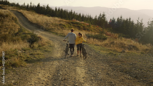 Guy and girl having walk with bicycles. Bicyclists looking around landscape