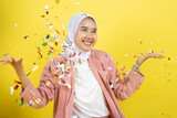 Beautiful young woman throwing confetti and looking happy on yellow background