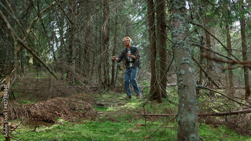 Man walking with trekking poles in green forest. Handsome guy trekking in woods