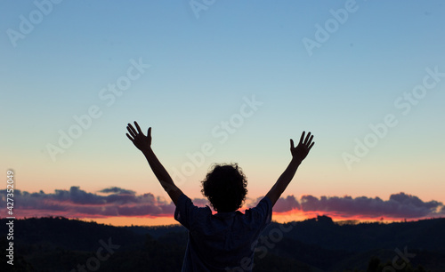 Young man with arms raised and feel grateful, with the sky just after sunset in the background. Concept of freedom, spirituality or happiness.
