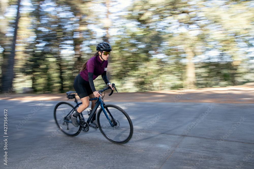 Obraz premium Mujer ciclista profesional a toda velocidad en una carretera en medio del bosque. Concepto de triatlón