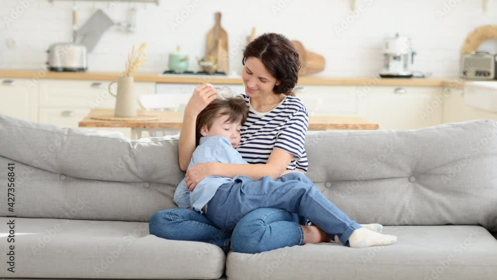Happy young mom sit on sofa embrace tired after funny games at home son sleeping on her hands. Lovely mother and little kid relationship. Spend leisure family time together in living room Happy young mom sit on sofa embrace tired after funny games at home son sleeping on her hands. Lovely mother and little kid relationship. Spend leisure family time together in living room