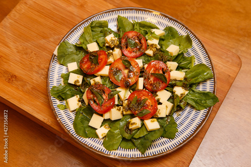 Deliciosa CAPRESE RUCULA, MUSSARELA DE BUFALA, TOMATES FATIADOS E MANJERICAO EM UMA SALADA COM PRATO NO FUNDO DE MADEIRA. photo