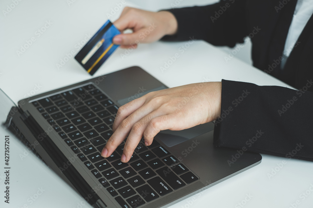 The businesswomen's hand is holding a credit card and using a laptop for online shopping and internet payment The businesswomen's hand is holding a credit card and using a laptop for online shopping and internet payment