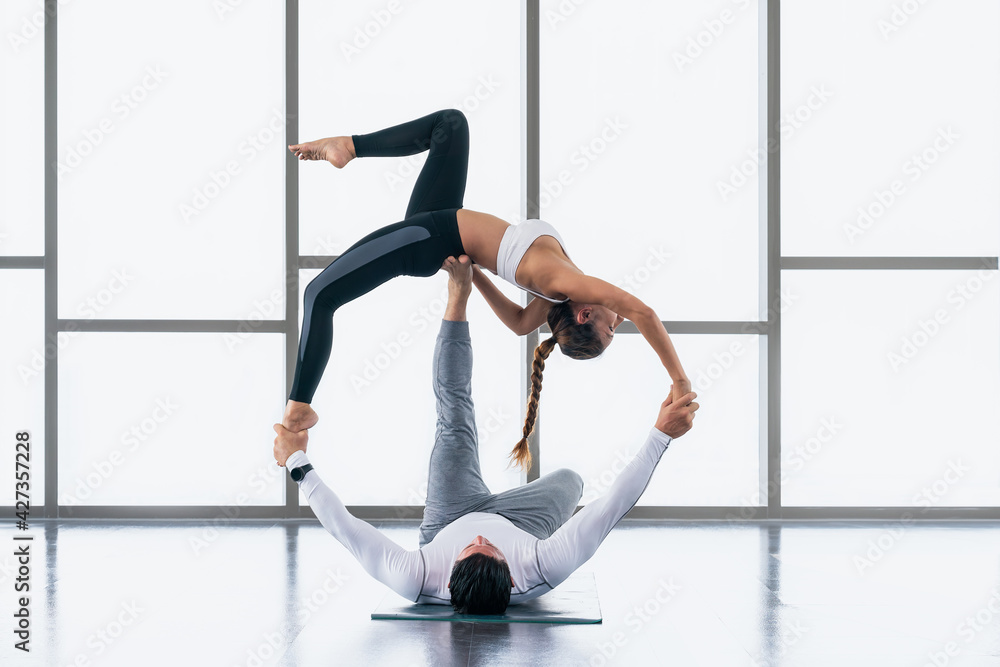 Obraz premium athletic couple practicing acro yoga or yoga partner together in gym