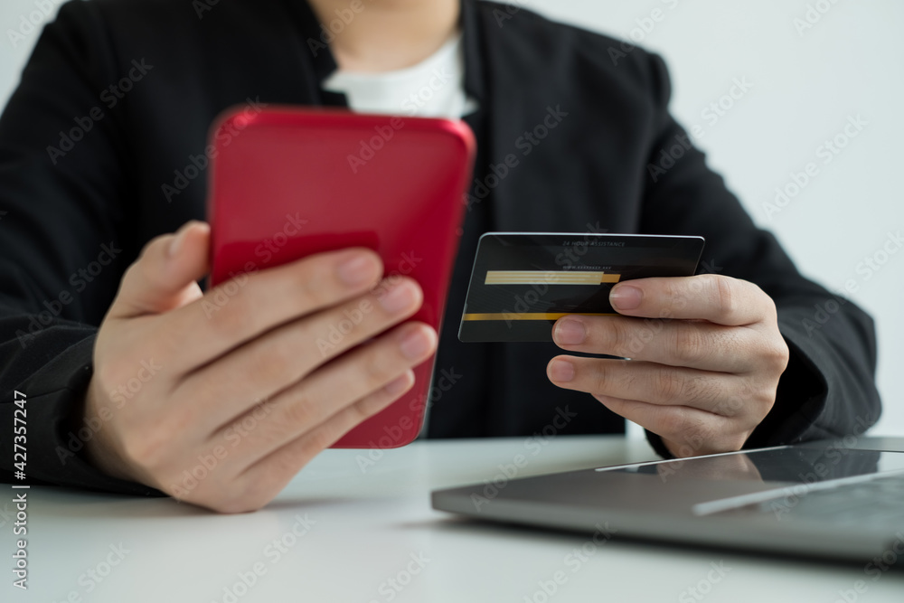 The businesswomen's hand is holding a credit card and using a smartphone for online shopping and internet payment in the office The businesswomen's hand is holding a credit card and using a smartphone for online shopping and internet payment in the office