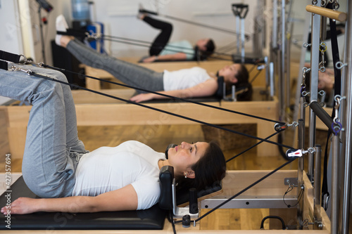 Young Hispanic woman performing set of pilates exercises on reformer in modern fitness studio © JackF