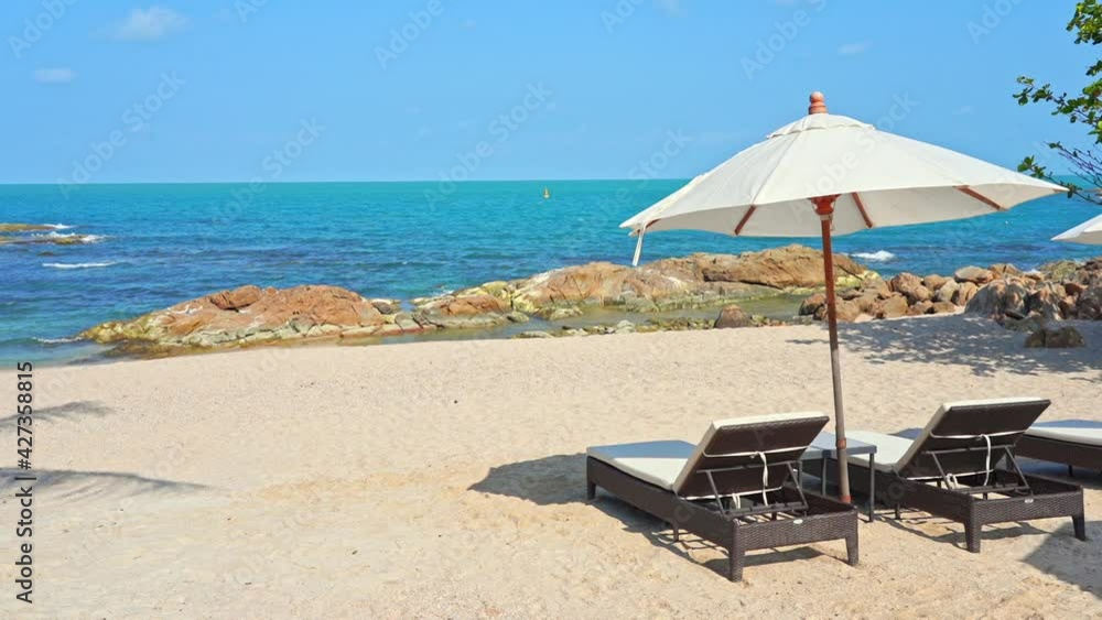 Two empty sun loungers under a sun umbrella facing a picturesque sandy beach and ocean view. Title space Two empty sun loungers under a sun umbrella facing a picturesque sandy beach and ocean view. Title space