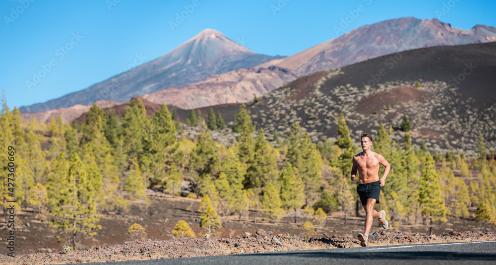 Fototapeta premium Sport athlete runner man shirtless running on mountain road in volcano mountain forest nature landscape. Summer outdoor training healthy active run lifestyle. Panoramic banner.