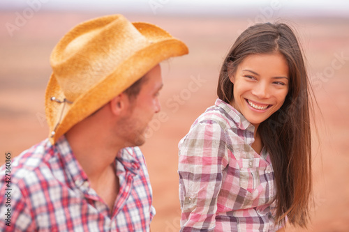 Couple people in western style portrait in american countryside farm. Smiling multiracial young interracial couple in USA nature. Man wearing cowboy hat and Asian woman wearing plaid shirt.