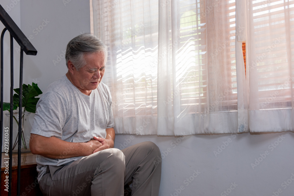 Asian senior man sitting alone on staircase at home with sickness. Stressed elderly male have stomachache and feel unwell need for medicine. Senior people health care and illness recovery concept Asian senior man sitting alone on staircase at home with sickness. Stressed elderly male have stomachache and feel unwell need for medicine. Senior people health care and illness recovery concept