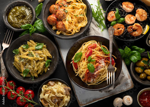 Assortment of Italian pasta with traditional sauces for dinner on dark background.