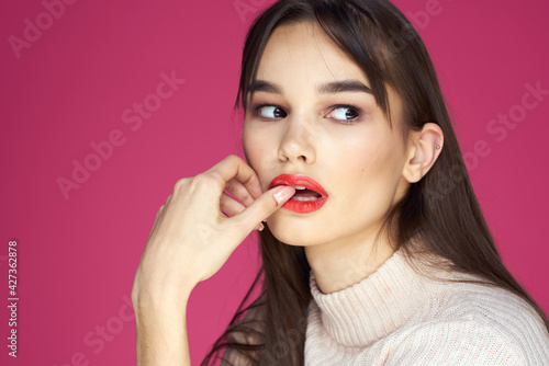 Brunette with long hair red lips cosmetics white sweater pink background cropped view