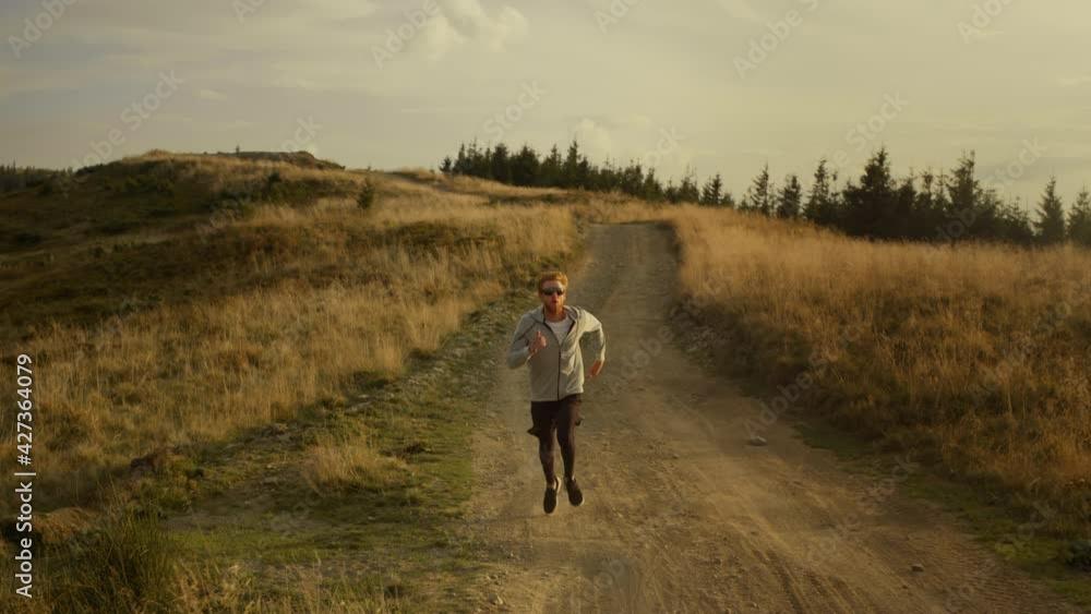 Fit guy running marathon in mountain landscape. Strong man jogging on dirty road Fit guy running marathon in mountain landscape. Strong man jogging on dirty road