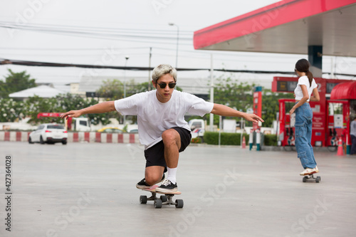 Asian young man skater riding on skateboard on courtyard at gas station with wear sunglasses. Young man skateboarding outdoor
