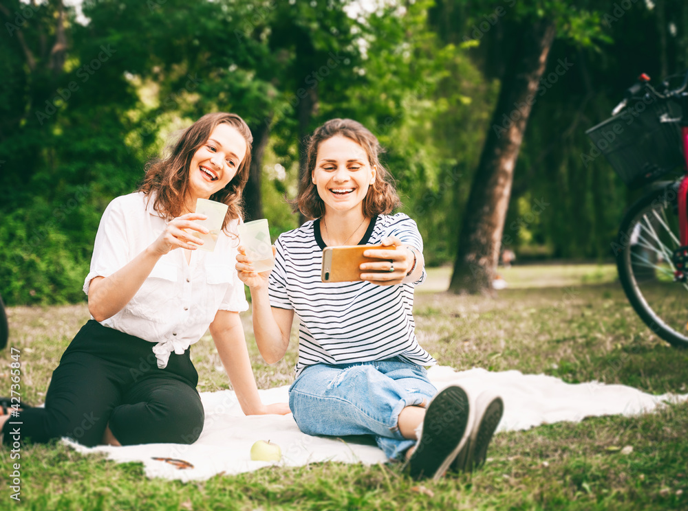 Two young beautiful women friends having fun in a summer park and making selfie, Friendship day